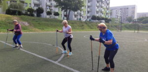 Grupa trzech osób ćwiczy na boisku z kijkami. 